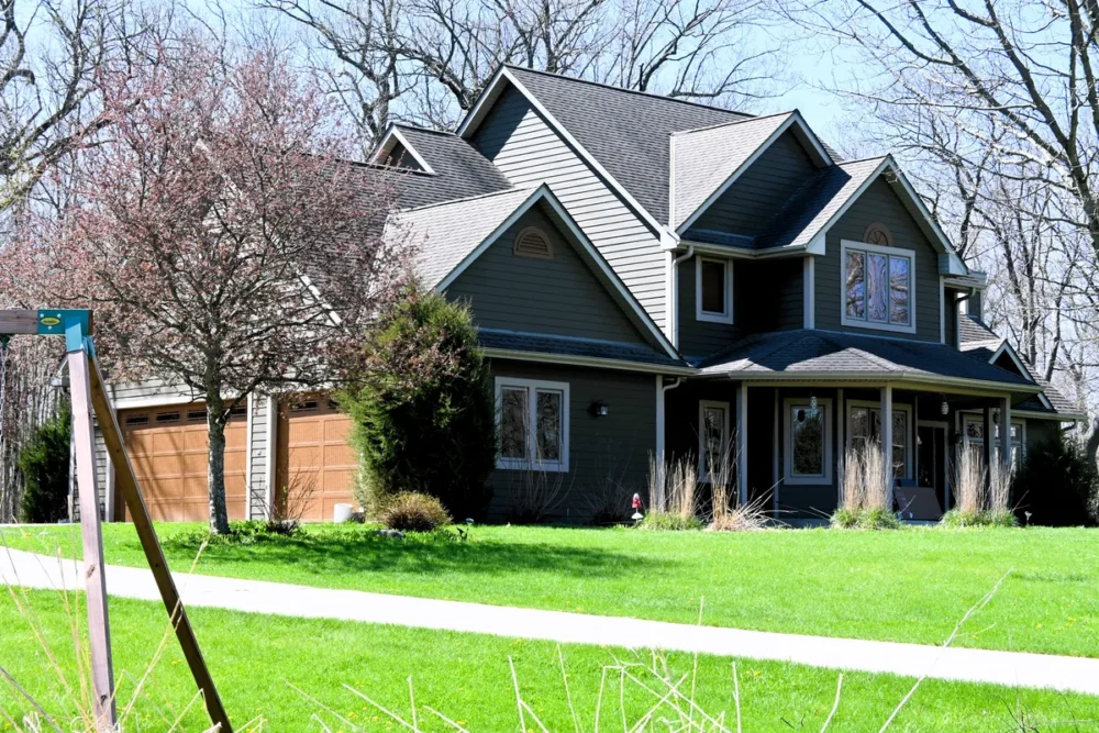 Exterior painting project on County Line Rd in Hartland WI featuring dark green-gray siding, white trim, natural wood garage doors, and a landscaped front yard.