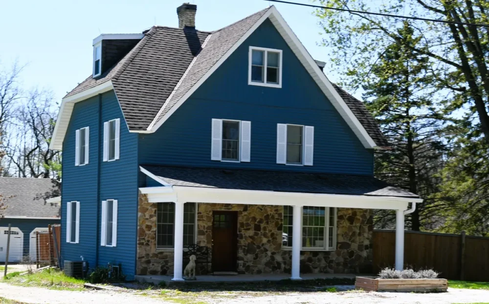 Exterior painting project on Nashotah Rd in Oconomowoc WI featuring blue siding, white trim, shutters, porch columns, and stone front entry.