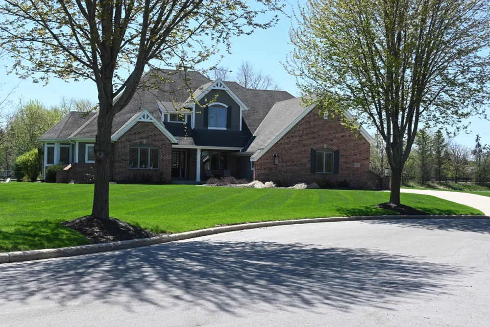 Exterior painting project on Switch Grass Ct in Hartland WI featuring a brick home with dark siding, white trim, gable accents, and a landscaped front yard.