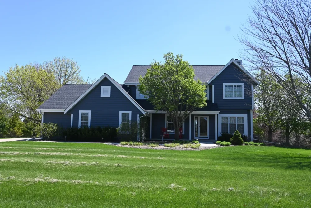 Exterior painting project on Hawthorne Ln in Hartland WI featuring dark siding, white trim, gable accents, front entry, and a large green lawn.