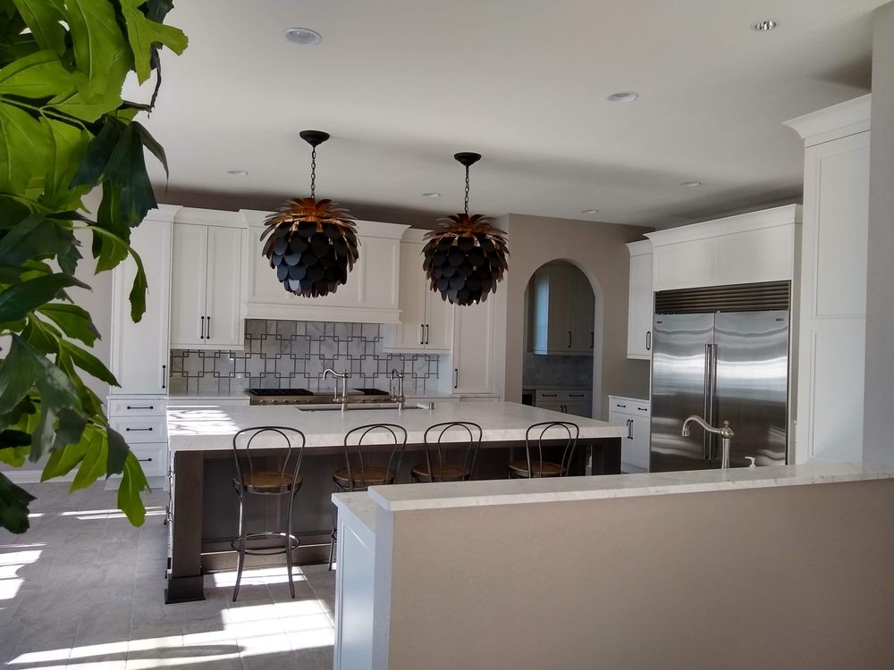White kitchen cabinets with a dark island, patterned backsplash and sculptural pendant lights