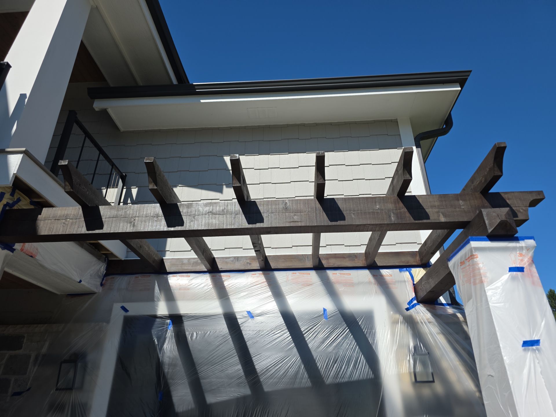 Windows and columns protected with plastic and painters tape beneath wood pergola beams
