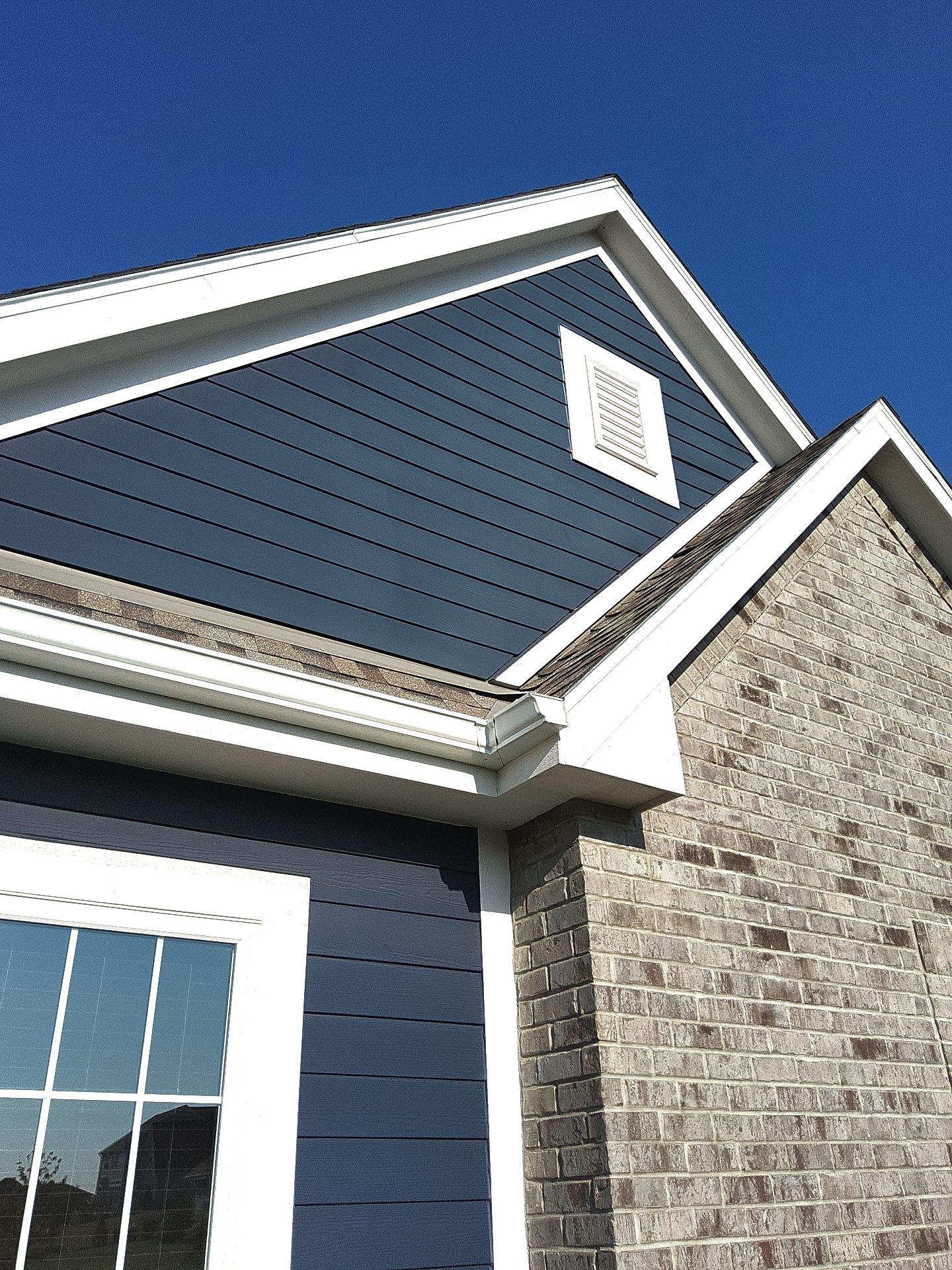 Deep blue exterior siding with white gable trim beside a brick facade