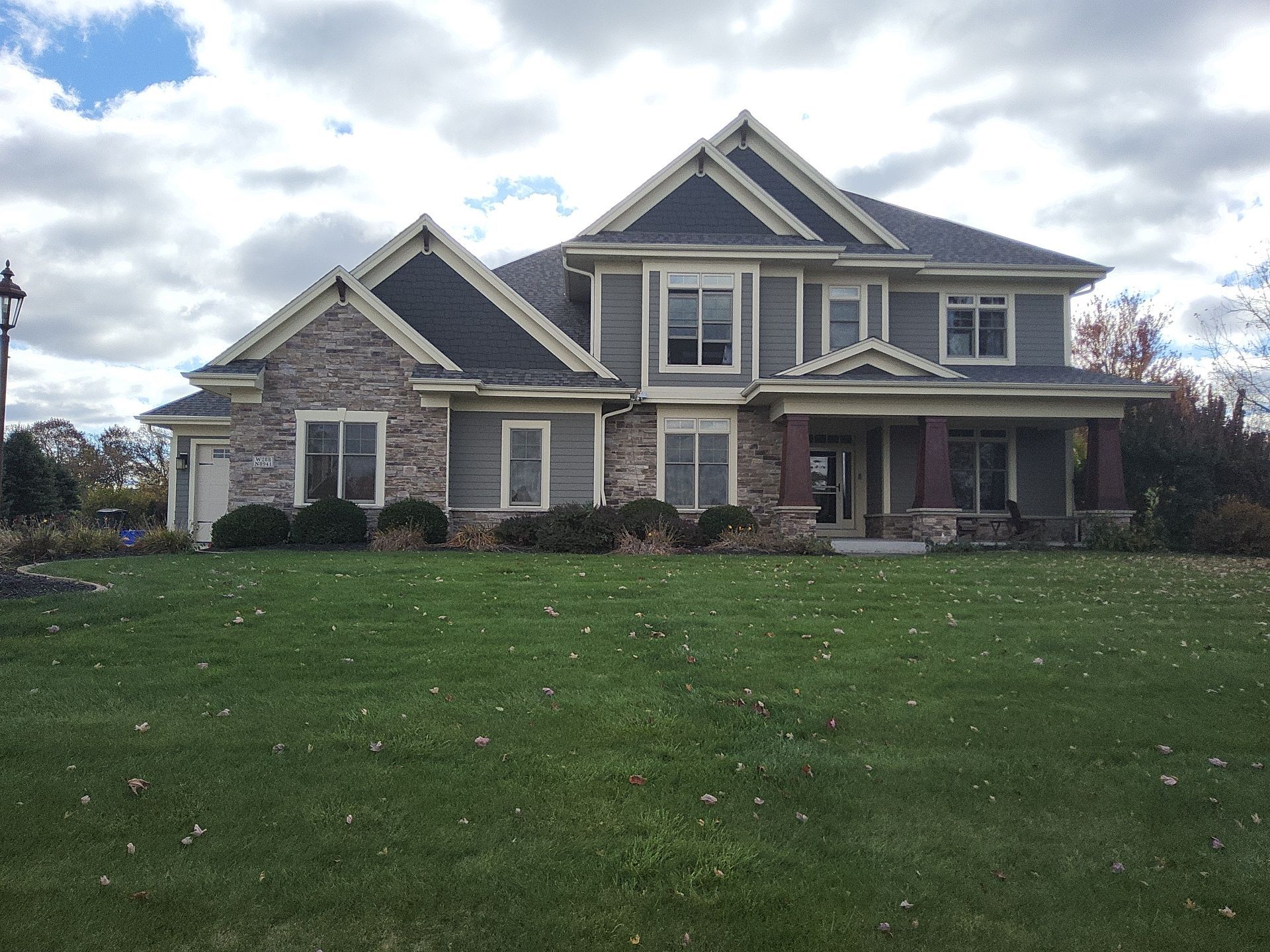 Full view of a finished home with gray siding, stone and light trim