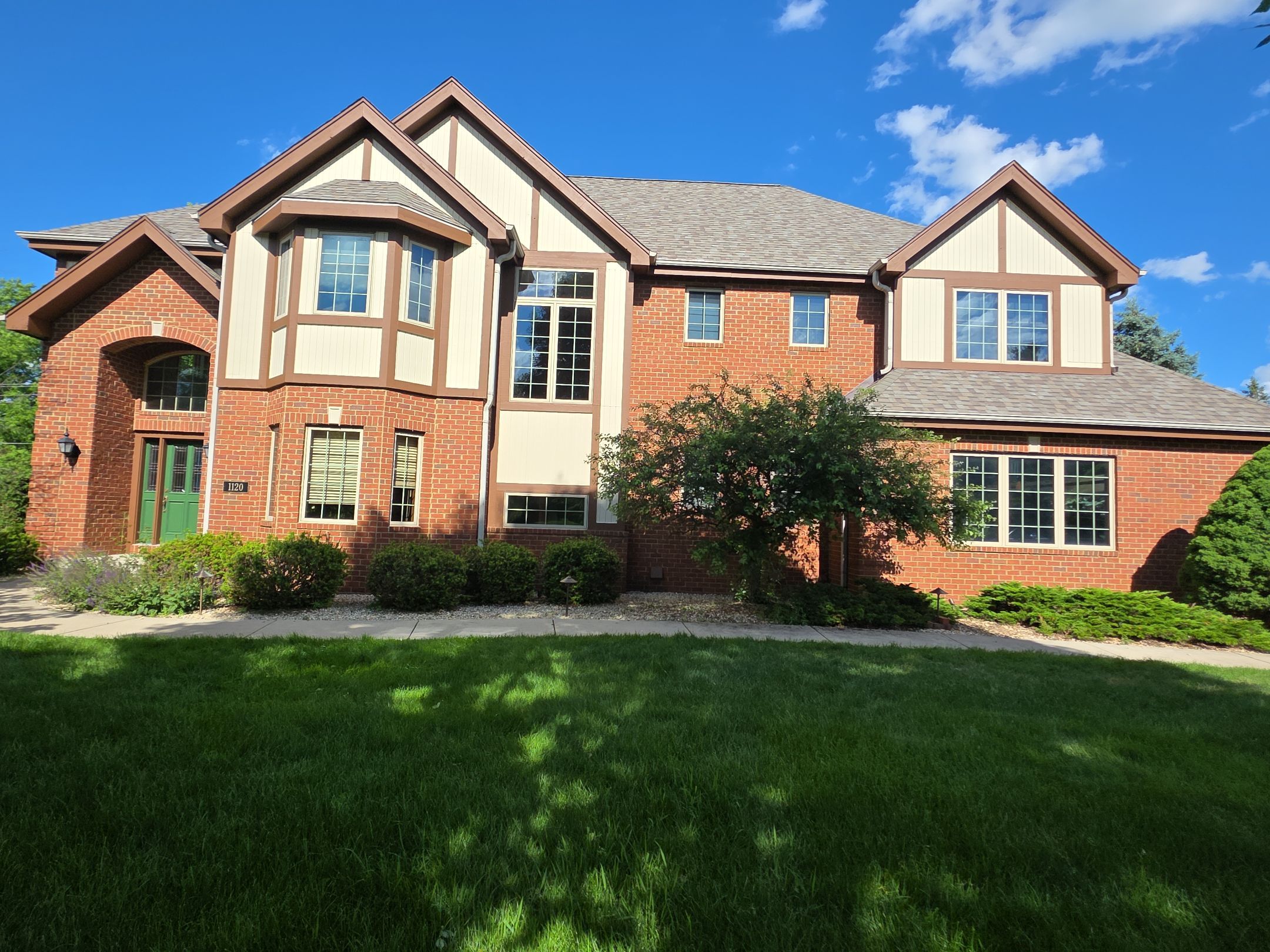 Brick Tudor home with freshly painted light siding and brown trim after painting