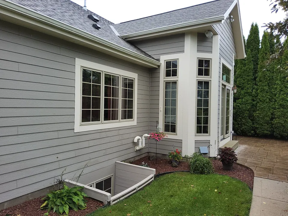 Rear exterior with gray siding and tall white-trimmed bay windows.