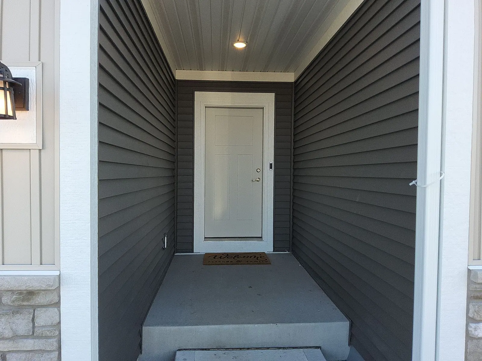 Covered entry with dark horizontal siding, a light door and recessed ceiling light.