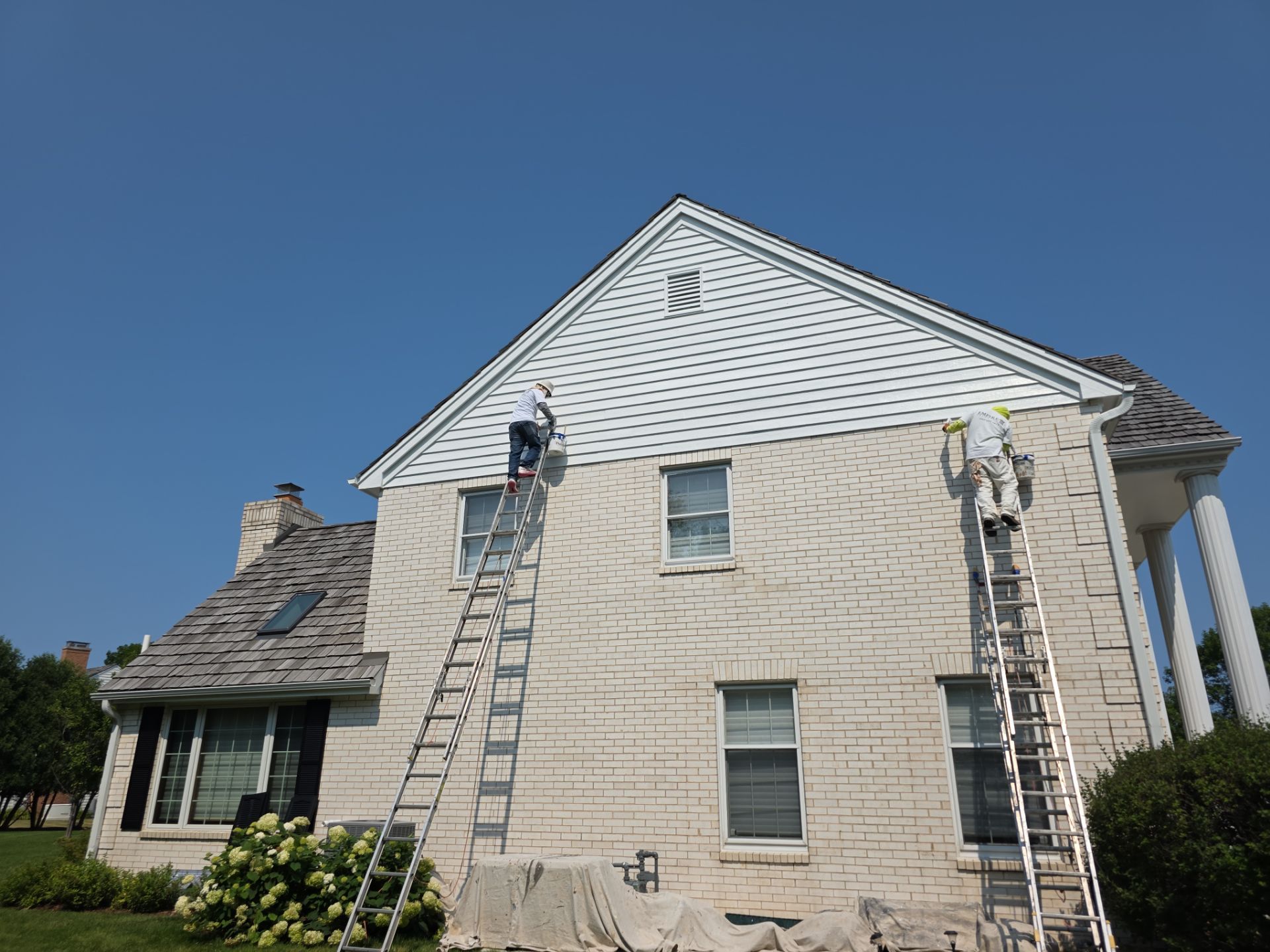 Empire painters working from ladders on a Mequon home exterior