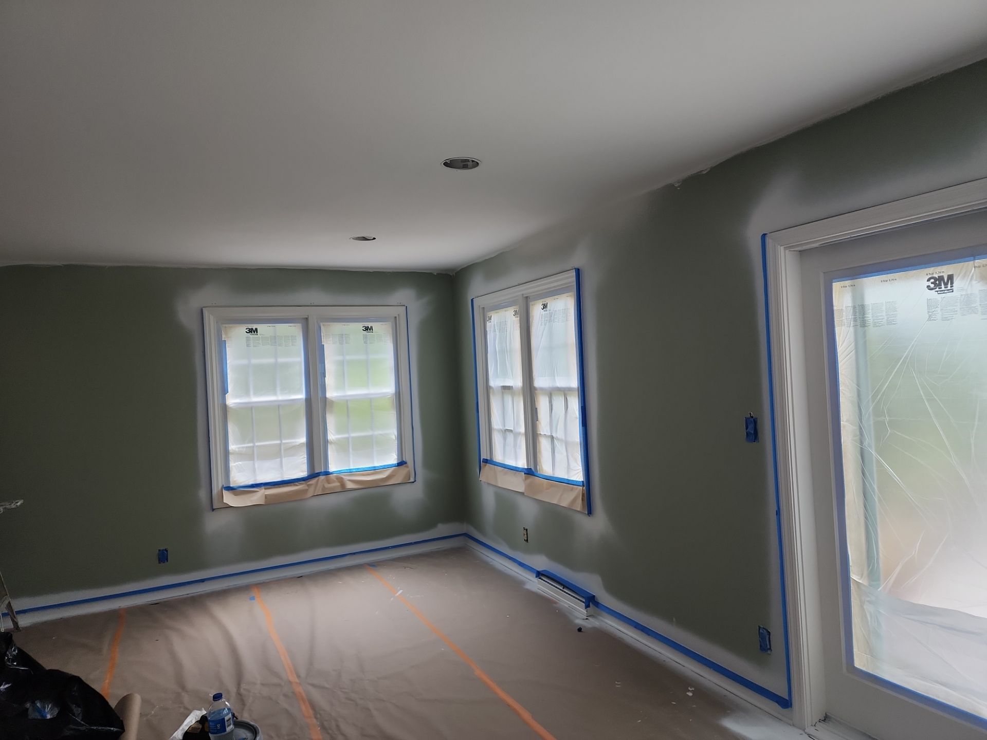 Interior painting preparation with windows covered in plastic and floors protected with paper