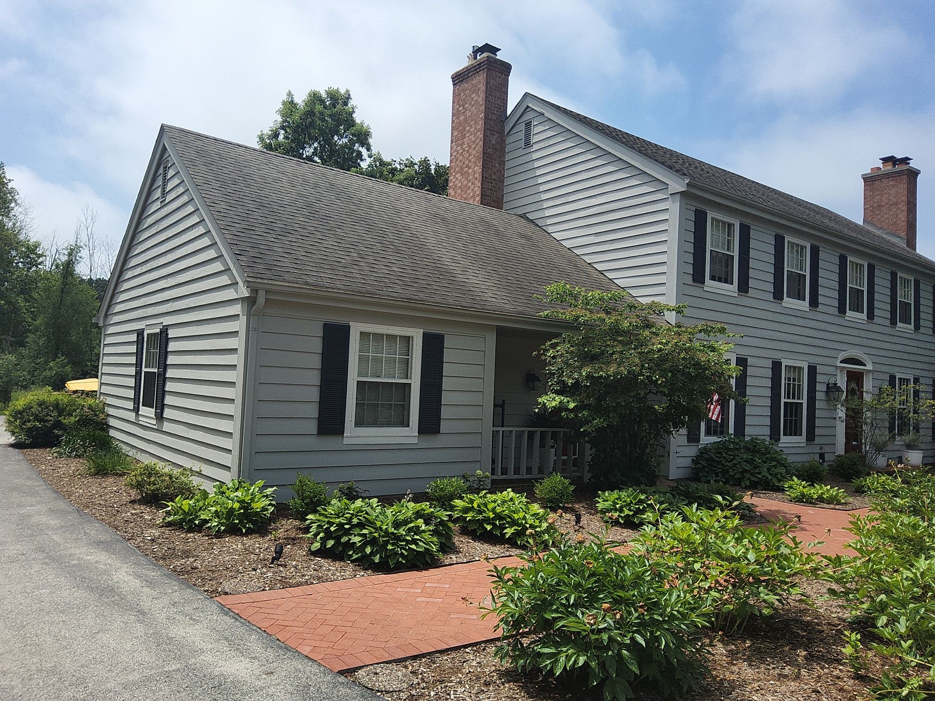 Mequon home on White Oak Way with light siding, dark shutters and red brick walkway