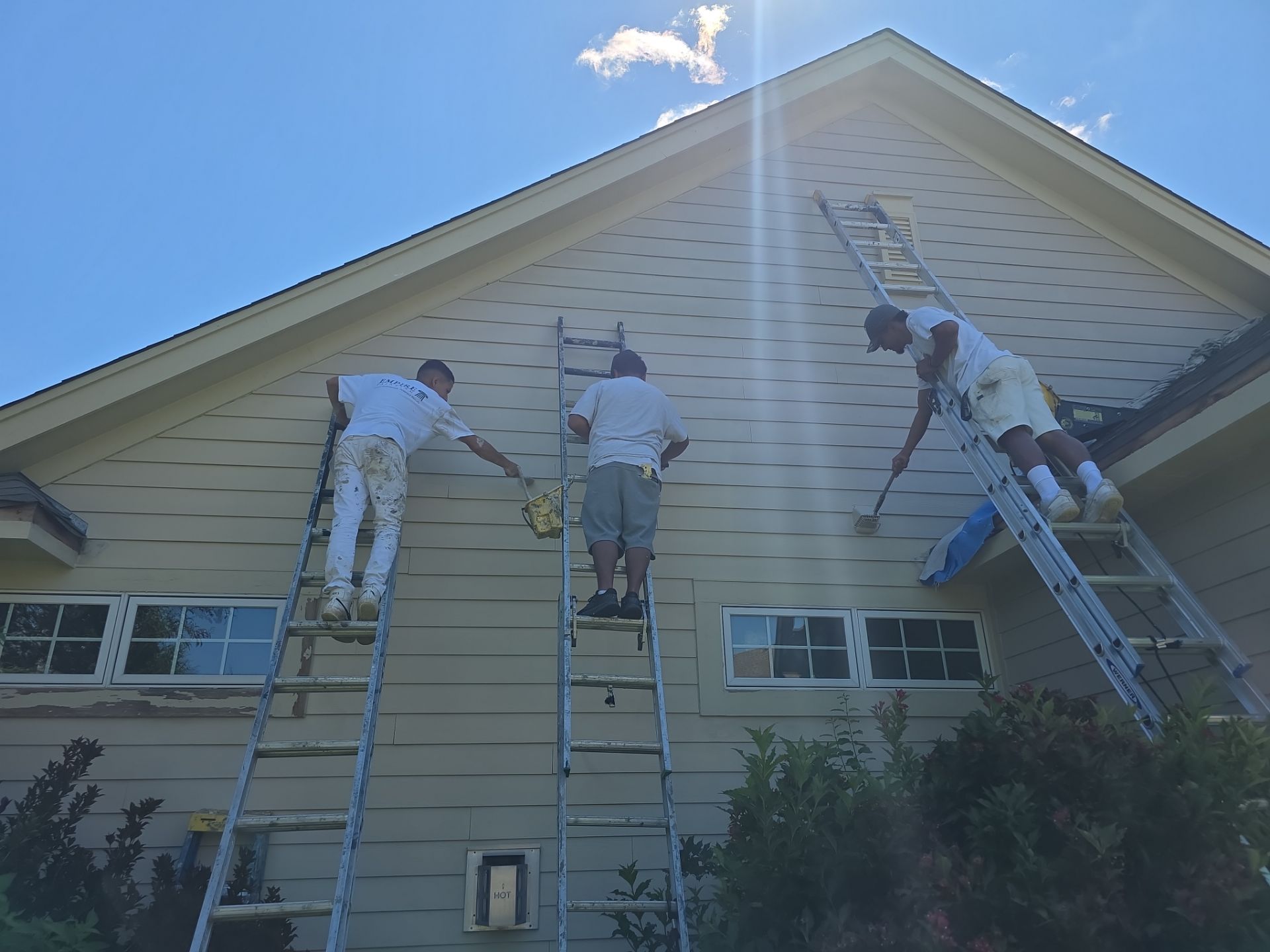 Three Empire Painting crew members working from ladders on exterior siding in Menomonee Falls