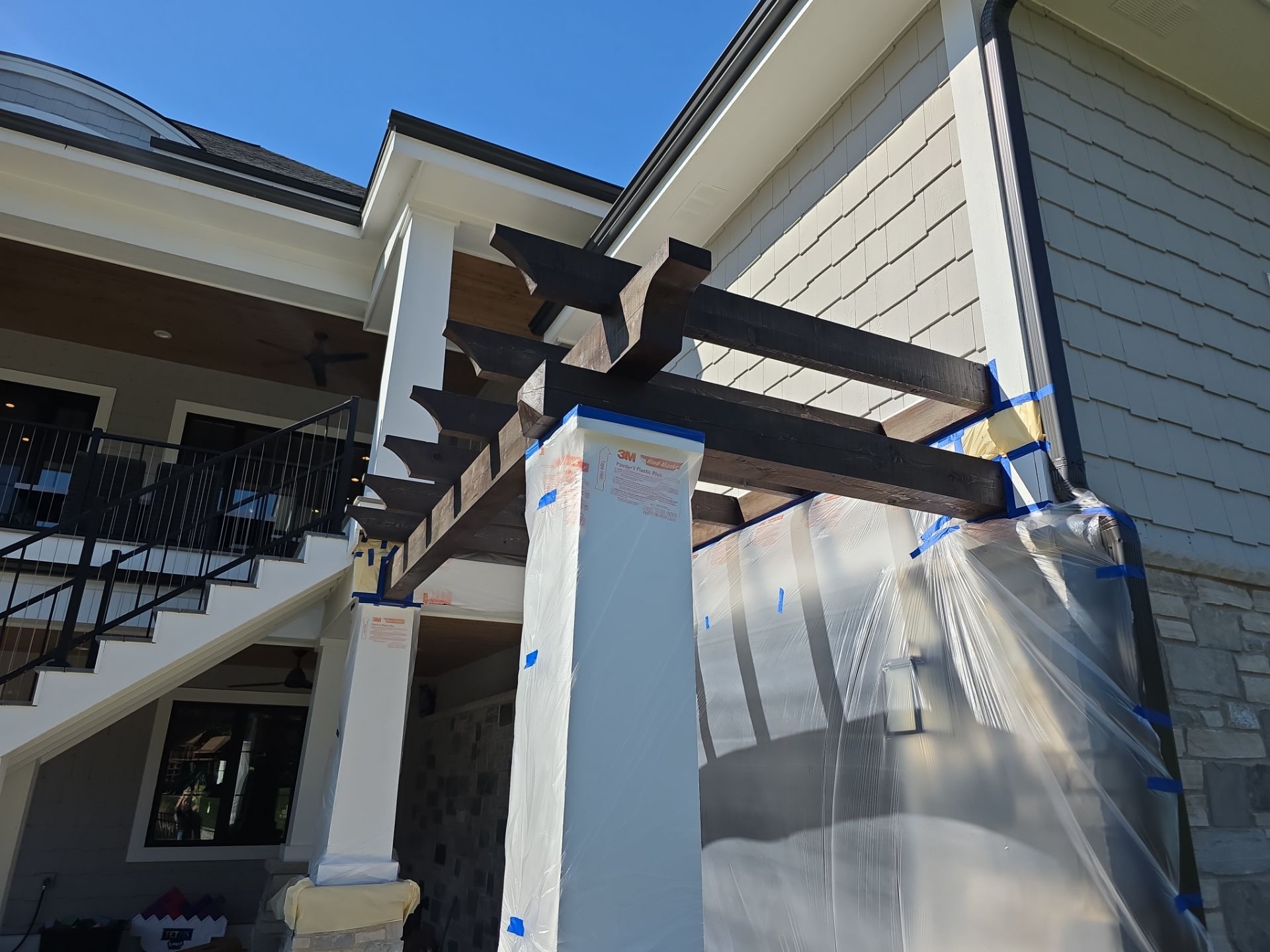 Pergola staining in progress with columns and adjacent surfaces masked