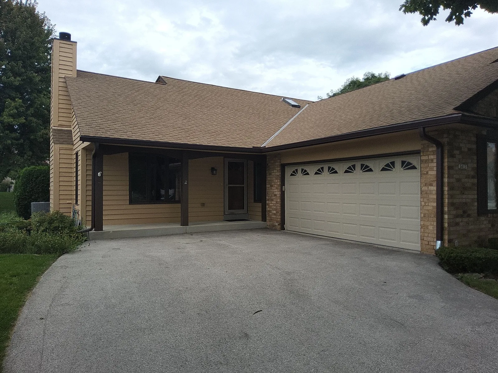 Finished Greenfield home exterior with warm tan siding, dark brown trim and a cream garage door