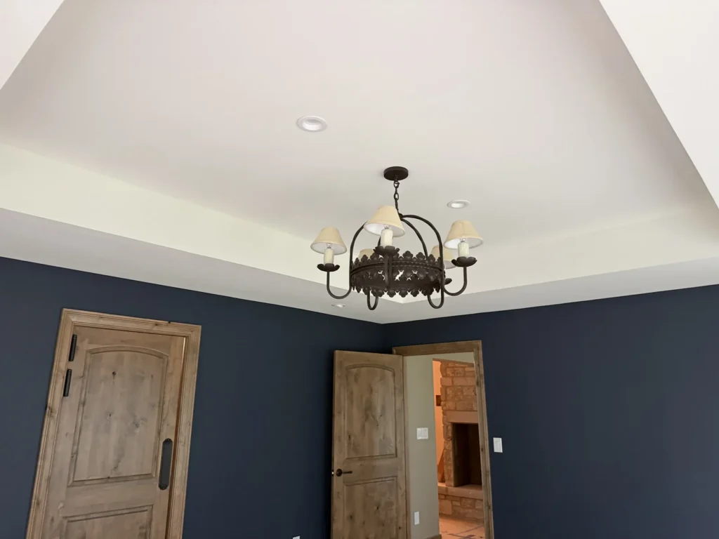 White tray ceiling and chandelier above deep blue walls and natural wood doors.