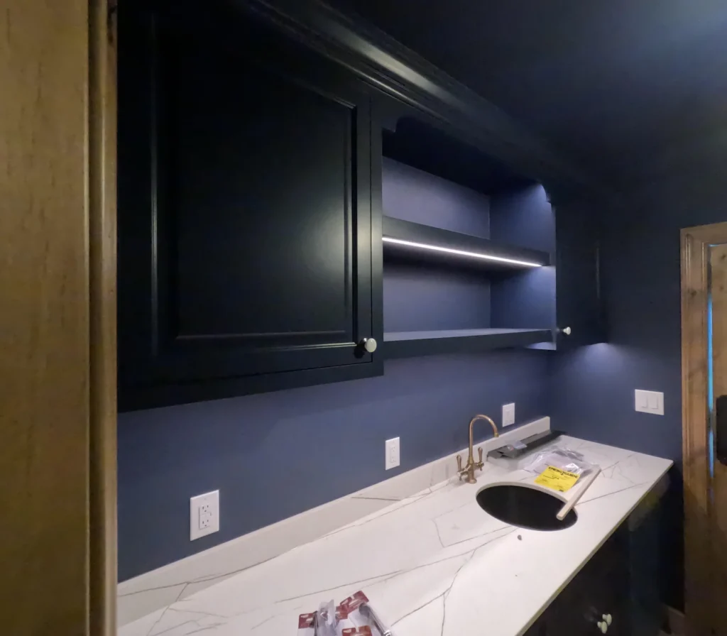Dark cabinetry and open shelves above a white counter against blue walls.