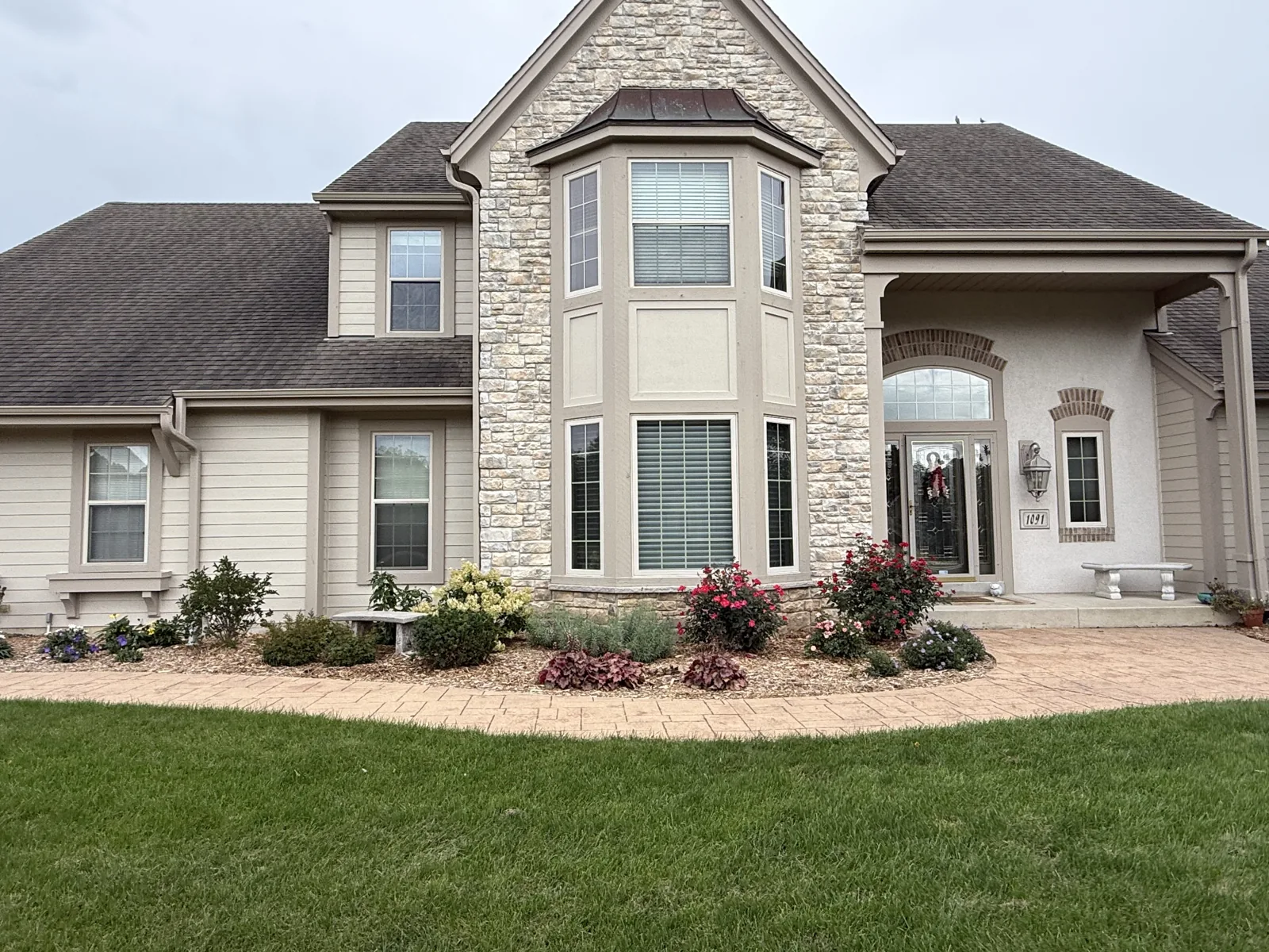 Light siding and taupe trim around a stone-front gable and entry at a Pewaukee home