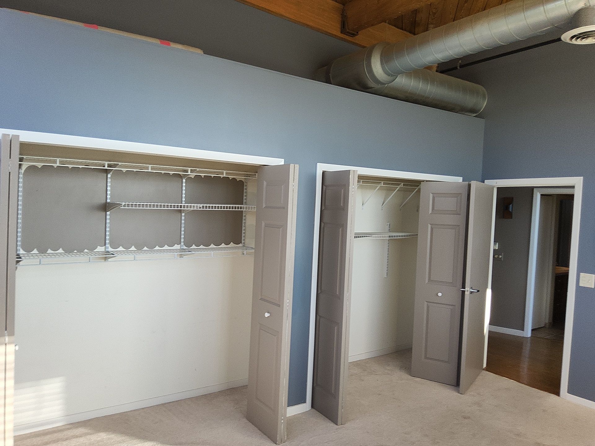 Blue-gray bedroom walls, white closet trim and gray doors beneath exposed timber and ductwork