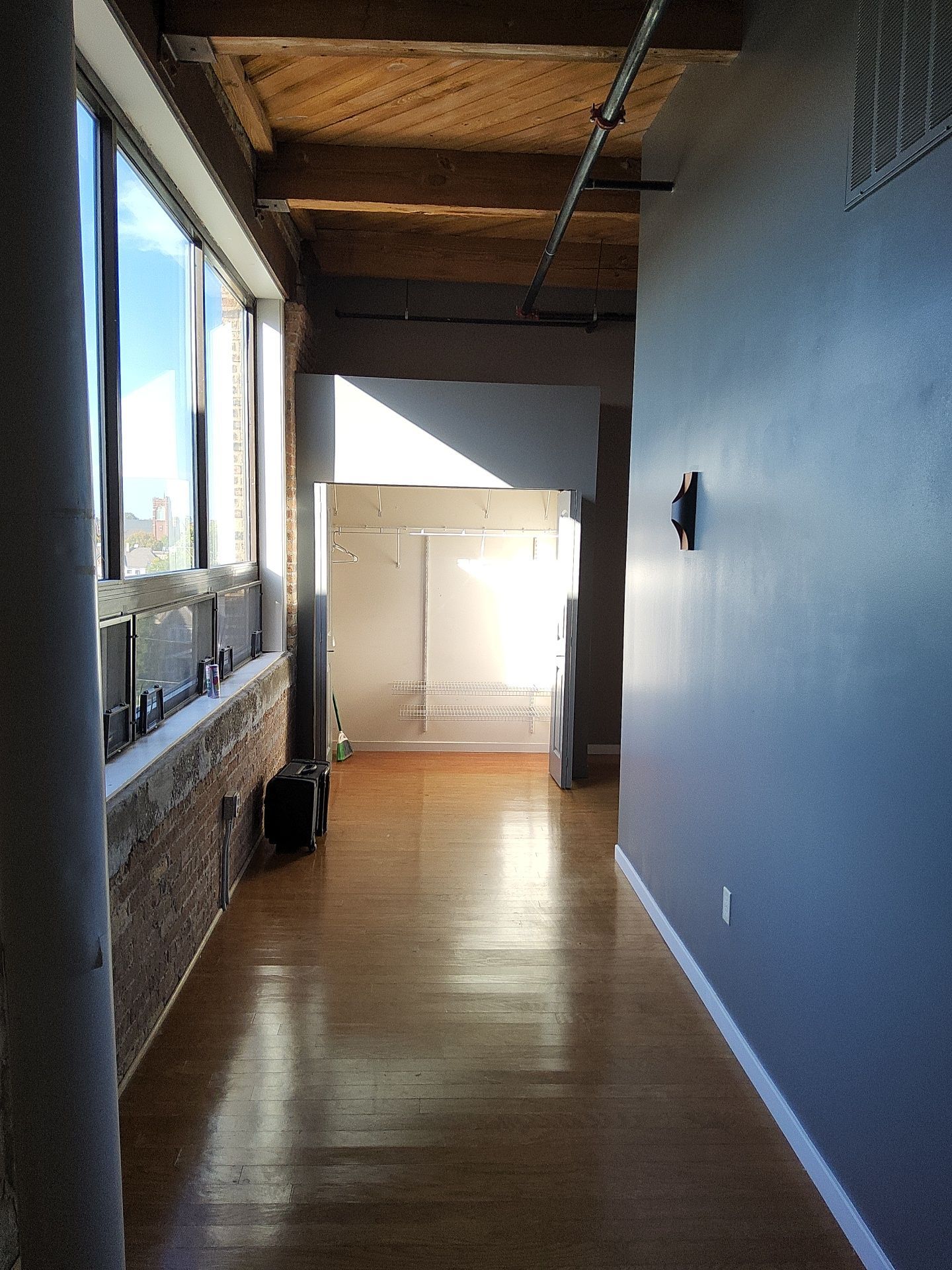 Sunlit loft hallway with blue-gray walls, white trim and exposed brick