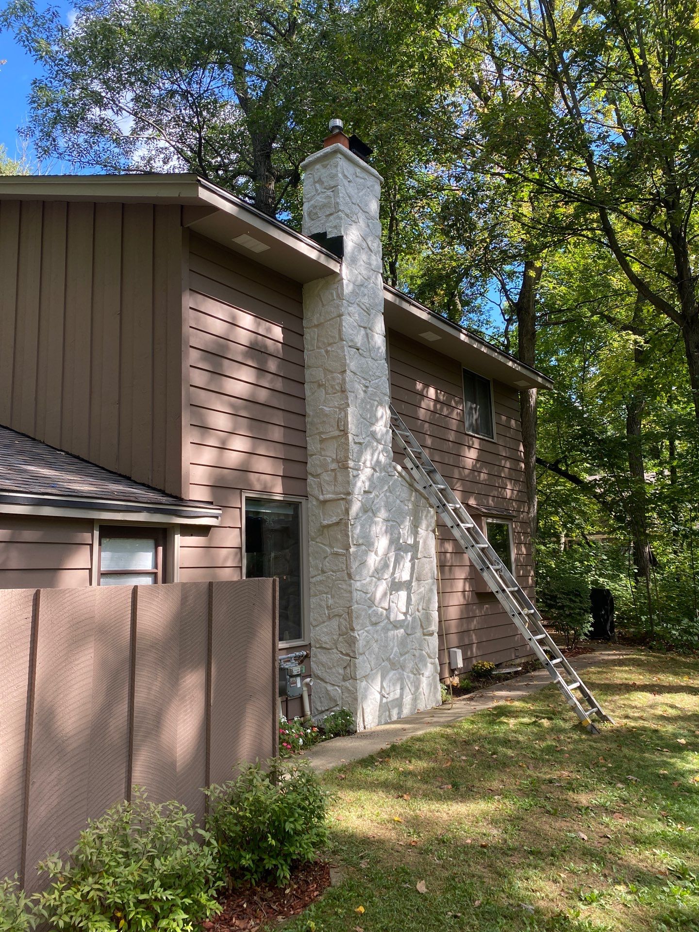 Colgate home exterior after painting with a white stone chimney and brown wood siding