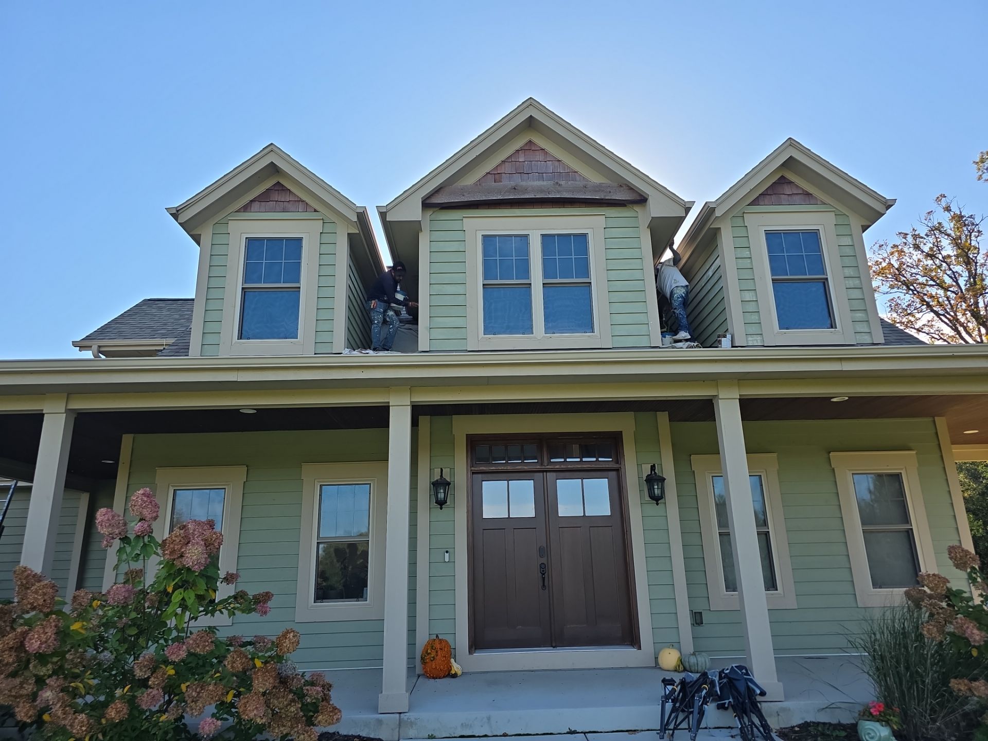 Crew working on a green Dousman home with three dormers and cream trim