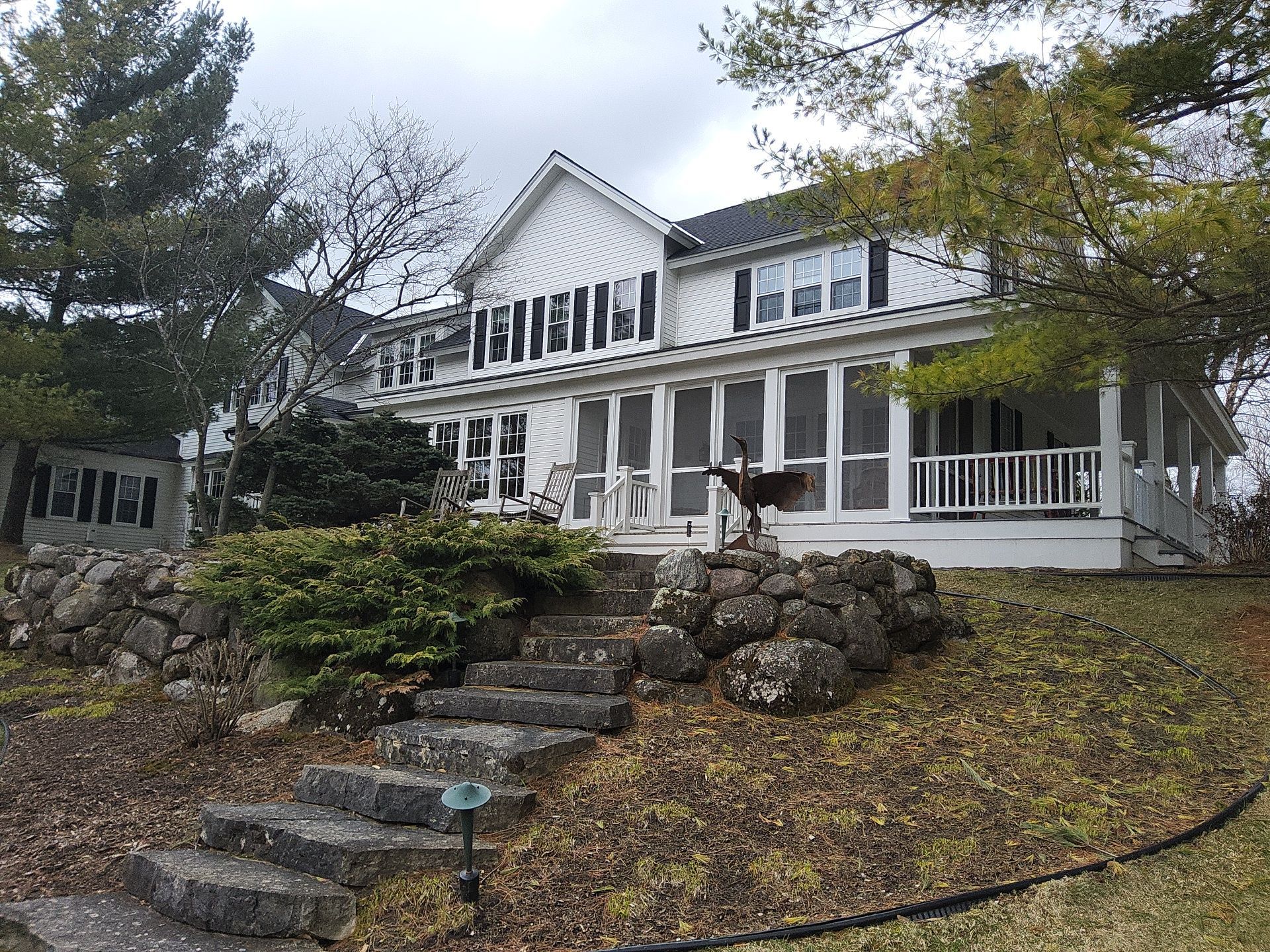 White Hartford home with black shutters, a broad screened porch and stone landscaping.